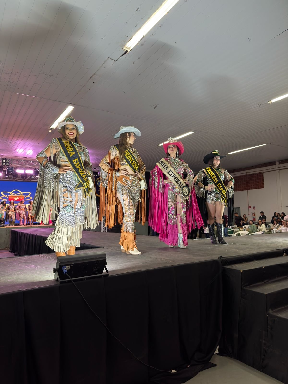 Baile da Rainha ExpoZal 2026 encanta o público com brilho, elegância e tradição em Sapezal No dia 06 de junho de 2026, Sapezal viveu um dos momentos mais aguardados da programação da ExpoZal: o tradicional Baile da Rainha ExpoZal 2026. O evento reuniu autoridades, patrocinadores, familiares e a comunidade para prestigiar um verdadeiro espetáculo de beleza, simpatia, desenvoltura e valorização da cultura sertaneja. Promovido pelo Lions Clube de Sapezal-MT, o baile foi marcado pela organização impecável e pela emoção que tomou conta do público durante os desfiles das candidatas. Com figurinos deslumbrantes, inspirados no universo country e repletos de brilho, franjas e detalhes sofisticados, as participantes transformaram a passarela em um show de elegância e personalidade. A Nova Corte da ExpoZal 2026 As candidatas demonstraram confiança, carisma e dedicação em cada apresentação, encantando os jurados e arrancando aplausos da plateia. Após desfiles de alto nível que evidenciaram o comprometimento e a beleza da mulher sapezalense, foram coroadas as grandes representantes da feira: • Rainha ExpoZal 2026: Destacando-se com um traje marcante em tom rosa vibrante e muito glamour. • Madrinha ExpoZal 2026: Encantando a passarela em um traje prata com detalhes impecáveis. • 1ª Princesa: Esbanjando simpatia em uma composição sofisticada em tons de caramelo. • 2ª Princesa: Fechando a corte oficial com muita elegância e brilho em seu traje escuro. Muito além da disputa pelos títulos, o baile celebrou a amizade, a integração e o espírito festivo que antecede uma das maiores festas do município. Tradição e Organização O Lions Clube de Sapezal, idealizador e promotor do evento, mais uma vez demonstrou seu compromisso com a valorização das tradições locais e com a realização de ações que fortalecem a cultura e o entretenimento da comunidade. O trabalho dedicado da entidade foi fundamental para proporcionar uma noite memorável, marcada pela emoção e pelo glamour. Com o sucesso do Baile da Rainha, cresce a expectativa para a programação da ExpoZal 2026, que promete reunir grandes atrações e movimentar a economia local, consolidando-se como um dos eventos mais importantes da região. O Baile da Rainha ExpoZal 2026 ficará na memória como uma celebração do talento, da beleza e da dedicação das candidatas, que abrilhantaram a noite e demonstraram o orgulho de representar Sapezal em uma das mais tradicionais festividades do município.